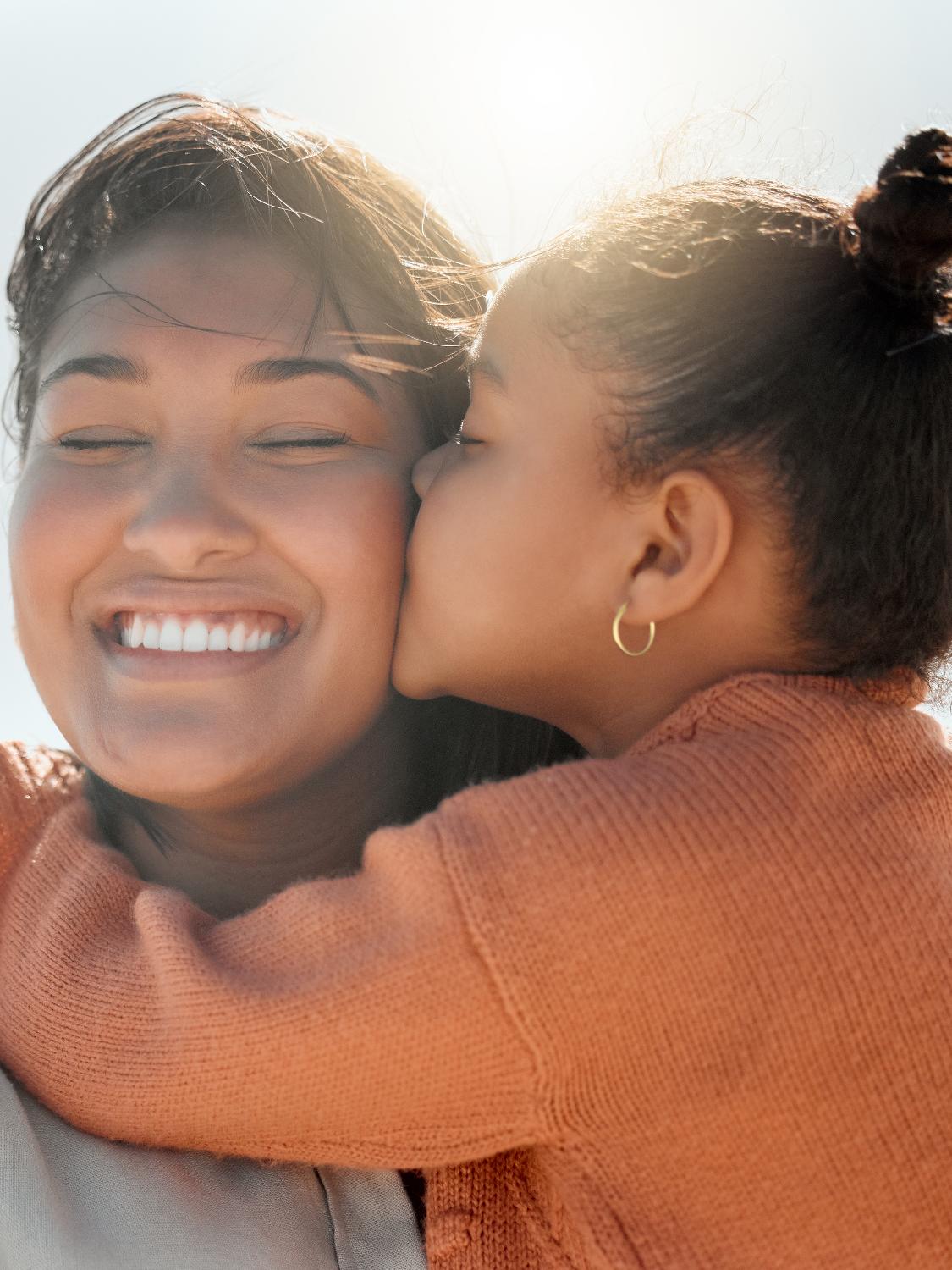 Kleines Mädchen mit Ohrringen gibt Mama einen Kuss auf die Wange - Momente des Schenkens | Emotionsbild