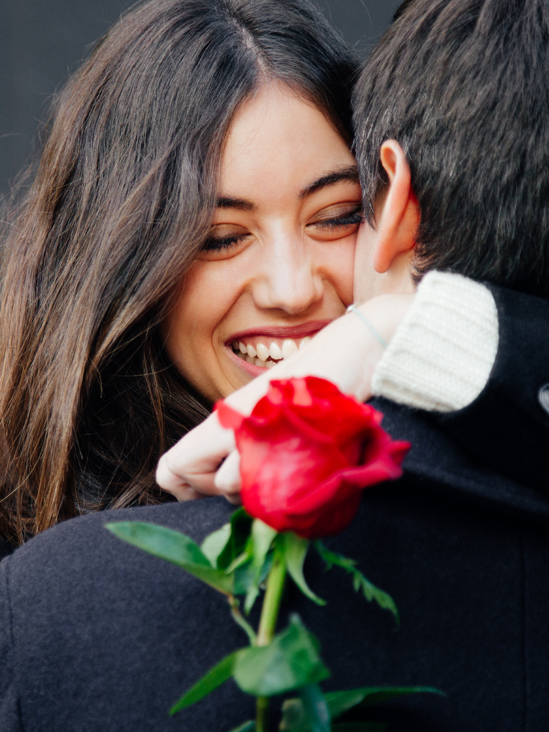 Frau mit Rose in der Hand umarmt herzlichen ihren Mann - Momente des Schenkens | Emotionsbild