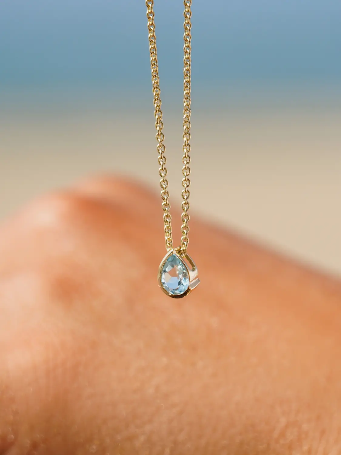 Damenanhänger aus echtem Gelbgold mit Blautopas Edelsteinen an Damenhand | Skintype