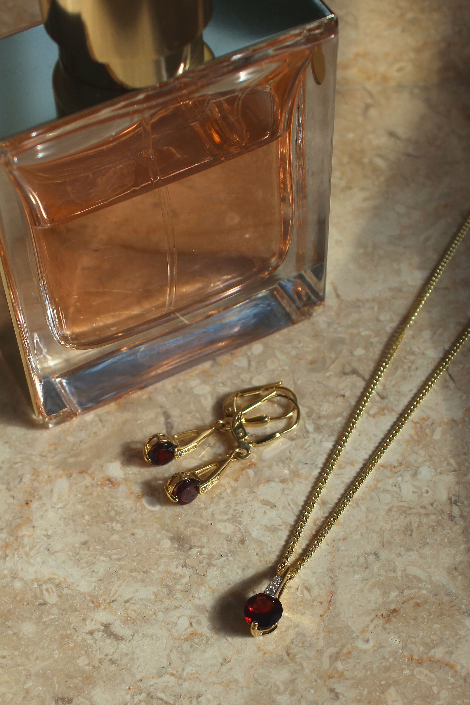 Damenanhänger und Damenohrringe aus echtem Gelbgold mit Granat Edelsteinen auf Marmor - Kaydence | Stilleben
